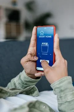 Multiracial man holding phone with program for smart home on the screen 写真素材