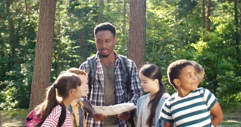 Multiracial man teacher standing in forest and examining route plan with her Stock Footage 162736641