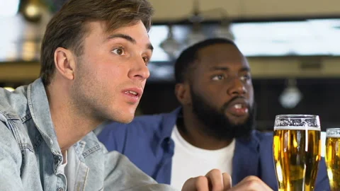 Multiracial men cheering for player scoring goal, relaxing in pub after work Stockbeeldmateriaal 104923609