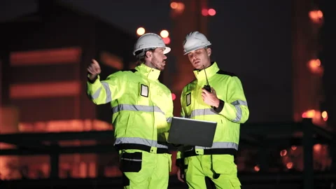 Multiracial refinery engineer points toward industrial structure beside Stock Footage 335607202