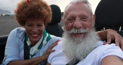 Multiracial senior couple having fun inside convertible car in summer vacation Stockbeeldmateriaal 153403268