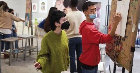 Multiracial students painting inside art room class wearing safety masks Видео 168622991