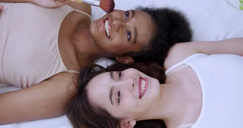 Multiracial teens lying together playing with makeup brush showing joy skincare Stock Footage 321936357
