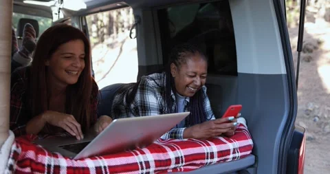 Multiracial women using computer laptop and mobile phone inside mini van camper Stock Footage 160537978