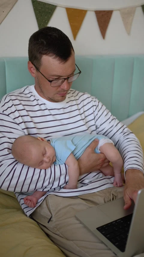 Multitasking father working on laptop from home office while holding his Video stock 344255938