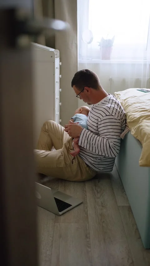 Multitasking father working on laptop from home office in bedroom while holding Stock Footage 344283844