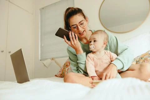 Multitasking mom taking a phone call while sitting with her baby Stock Photos