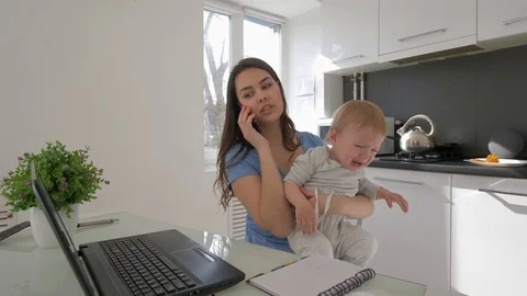 Multitasking mother with crying baby boy while working on laptop computer and Stock Footage 106178511