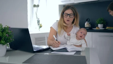 Multitasking mother with crying infant in arms sits at table on background of Stock Footage 91196621