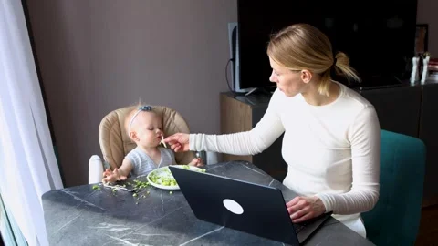 Multitasking mother feeding baby while working on laptop at home, parenting and Stock Footage 311755420