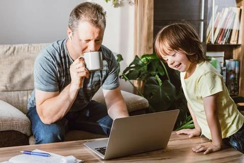 A multitasking young father tries to work from home with his son. A man checks Stock Photos