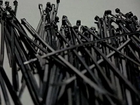 A multitude of dark, flexible nylon cable ties are scattered across a light.. Stock Photos