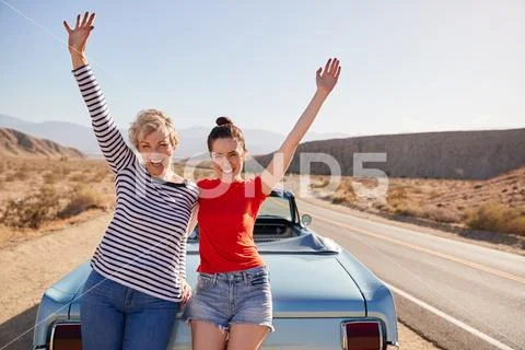 Mum and adult daughter on road trip stand waving to camera Stock Photos