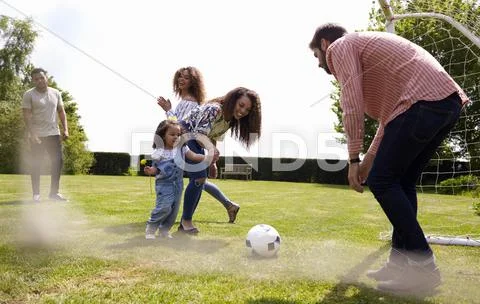 Mum And Friends Kicking A Ball Outdoors With Her Daughter