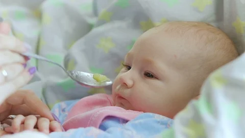 Mum feeds with a spoon her cute newborn baby puree of zucchini closeup Stock Footage 96738629
