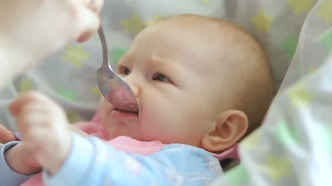 Mum feeds with a spoon her cute newborn baby puree of zucchini closeup Stock Footage 99831415