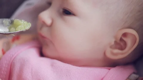 Mum feeds with a spoon her cute newborn baby puree of zucchini closeup Stock Footage 108310437