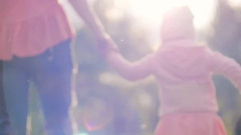 Mum holding daughter's hand going across grass Backlight bright sun shining at Stock Footage 108711698