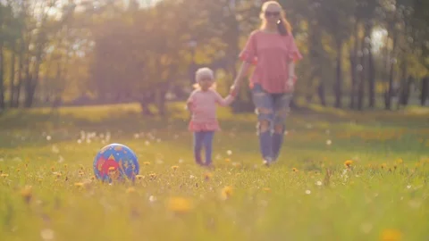 Mum holding daughter's hand going across grass Backlight bright sun shining at Stock Footage 108864243