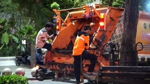 Municipal sanitation workers operate the compactor mechanism of a garbage truk Stock Footage 337300439