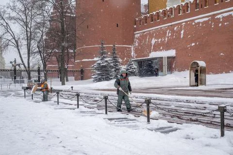 Municipal workers remove snow next to a soldier at a post near the Kremlin wall. Stock Photos