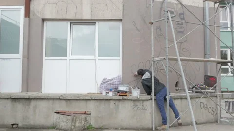 Mural on building wall, scaffold, tilt down to guy who spraying graffiti. Vídeos de archivo 57170802