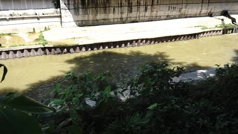 Murky water flows alongside a concrete retaining wall and a wooden barrier Stock Footage 345182136