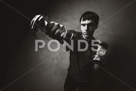 Muscle man posing with dumbbells on wall backdrop. Black and white photo Stock Photos