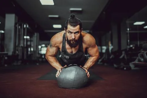 Muscled bearded man doing push ups from ball in gym. Stock Photos