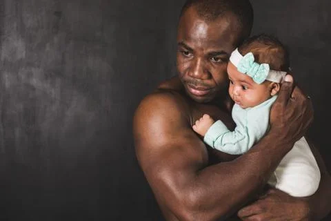 Muscular African American man holding a child against a black wall Stock Photos