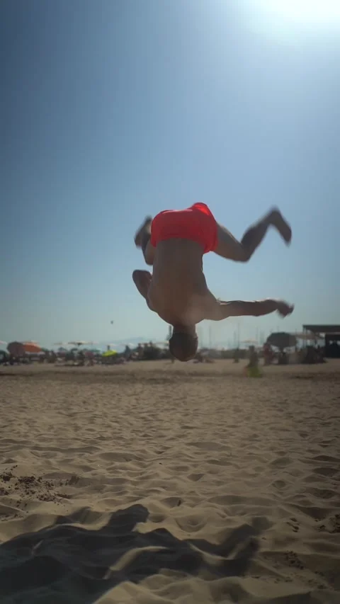 Muscular athlete doing an acrobatic backflip in slow motion on the sand. Young Stock-Footage 329164092