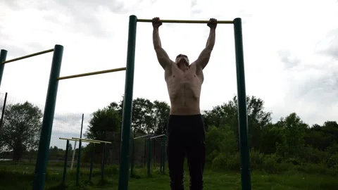 Muscular athlete doing pull ups on horizontal bar at sports ground. Young shirtl Stock Footage 303661230