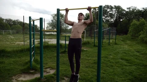 Muscular athlete doing pull ups on horizontal bar at sports ground. Young Stock Footage 309298138