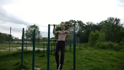 Muscular athlete doing pull ups on horizontal bar at sports ground. Young shirtl Stock Footage 340904138