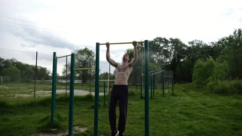 Muscular athlete doing pull ups on horizontal bar at sports ground. Young shirtl Stock Footage 344041376
