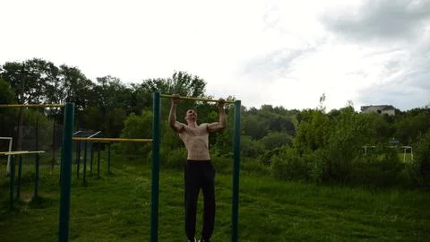 Muscular athlete doing pull ups on horizontal bar at sports ground. Young shi Stock Photos