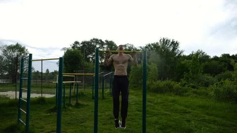 Muscular athlete doing pull ups on horizontal bar at sports ground. Young shi Stock Photos