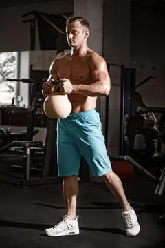 Muscular bodybuilder guy doing exercises with weight in gym Stock Photos