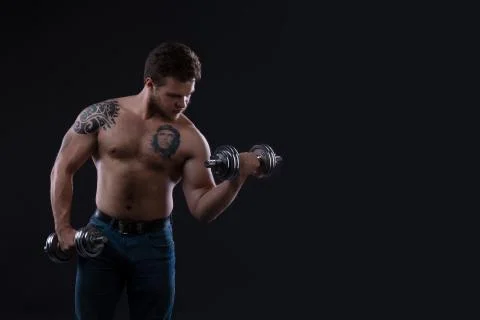 Muscular bodybuilder guy doing exercises with dumbbells over black background Stock Photos