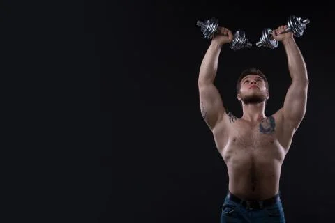 Muscular bodybuilder guy doing exercises with dumbbells over black background Stock Photos
