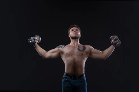 Muscular bodybuilder guy doing exercises with dumbbells over black background Stock Photos