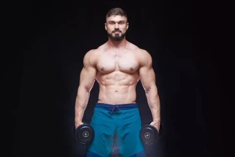 Muscular bodybuilder guy doing exercises with dumbbell over black background Stock Photos