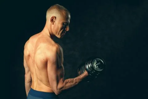 Muscular bodybuilder guy doing exercises with dumbbell over black background Stock Photos