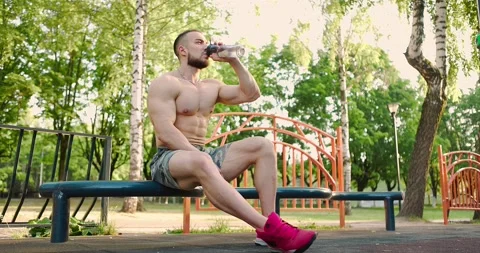 Muscular bodybuilder taking break during workout in city park.Man drinking Video stock 157188100