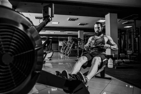 Muscular fit man using rowing machine at gym Stock Photos