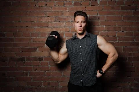 Muscular guy doing exercises with dumbbell against a brick wall Stock Photos