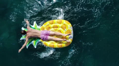 Muscular guy in pink swimming trunks lies on orange pineapple-shaped inflatable Stock Footage 138608024