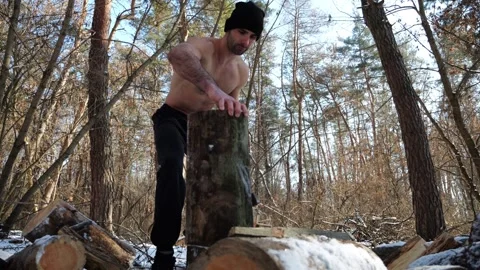 Muscular guy placing a log on a stump in a winter forest. Shirtless young man pr Stock Footage 328125655