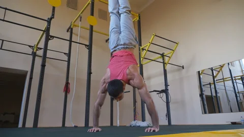 Muscular gymnast doing push ups in handstand at gym. Young athlete doing stunts Stock Footage 153662976
