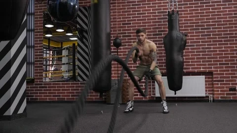 A muscular male boxer does an exercise with ropes in a sports gym. Stock Footage 150357092
